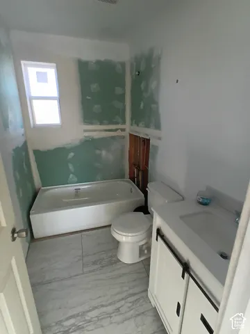 Bathroom featuring large-format tile flooring, a white vanity with a rectangular integrated sink, a standard toilet, and a white soaking tub