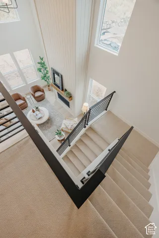 Staircase featuring wall-to-wall carpeting and black metal railings with wooden handrails, overlooking a double-height ceiling space with floor-to-ceiling vertical plank wall detailing and multiple windows