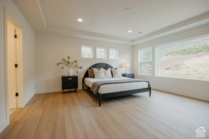 Bedroom featuring wood-finish flooring, recessed tray ceiling, recessed lighting, and large picture windows showcasing mountain scenery