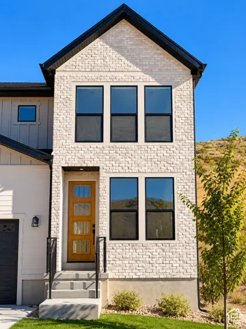 Exterior facade featuring white brick masonry, wood-finish front door with glass panels, dark-toned window frames, and black metal handrails