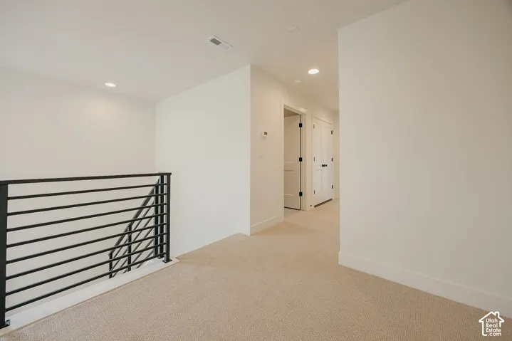 Neutral-toned carpeting, minimalist black horizontal metal stair railing, recessed ceiling lighting, and solid-core interior doors with matte black hardware