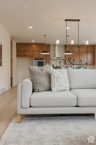 Kitchen featuring flat-panel wood-finish cabinetry, stainless steel wall-mounted oven, stainless steel range hood, and recessed lighting, complemented by wood-finish flooring