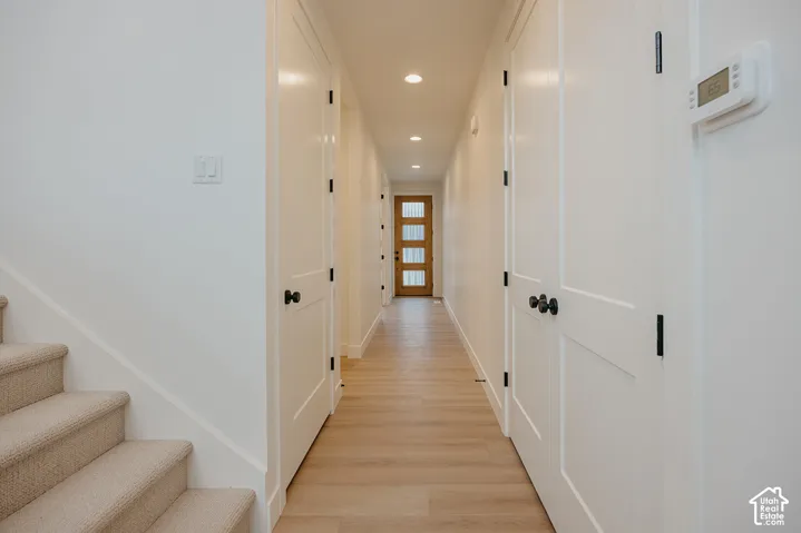 Hallway featuring wood-finish flooring, recessed lighting, shaker-style interior doors with matte black hardware, and a four-panel door with glass inserts