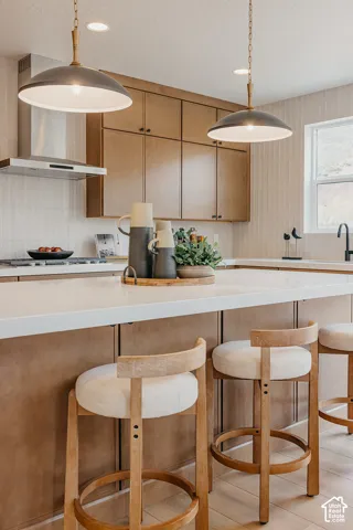 Kitchen featuring flat-panel wood cabinetry, quartz countertops, dual pendant lighting, stainless steel range hood, and vertical tile backsplash
