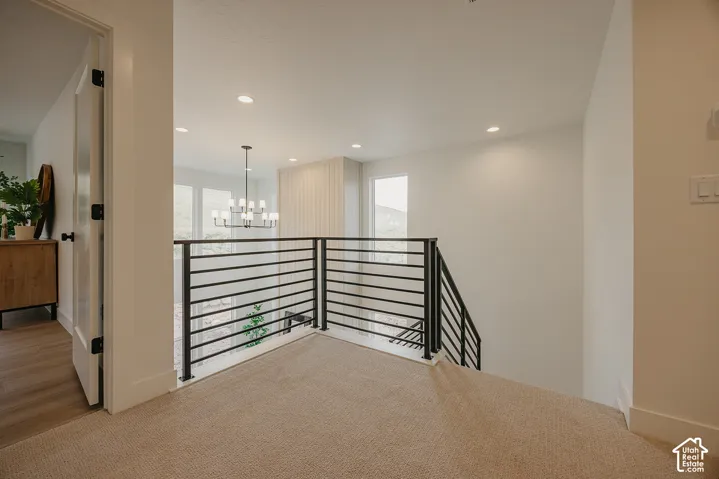 Black metal horizontal railing, recessed ceiling lighting, vertical panel wall accent, and multi-tier pendant chandelier