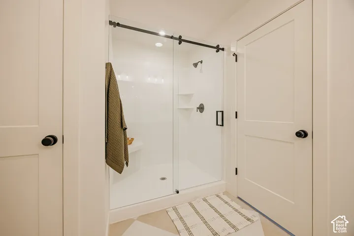 Walk-in shower featuring a frameless glass sliding door, matte black hardware, integrated shelving, and a built-in corner seat