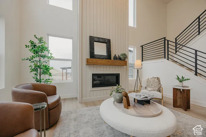 Double-height ceilings, floor-to-ceiling vertical plank fireplace surround, natural wood mantel, wood-finish flooring, and metal railing staircase