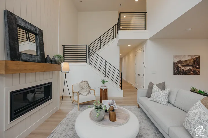 Double-height ceilings with vertical shiplap fireplace surround, linear gas fireplace with wood mantel, and staircase featuring horizontal black metal railings
