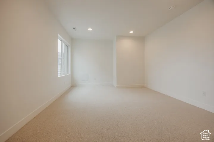 Neutral interior room featuring neutral-tone carpeting, smooth white walls, recessed ceiling lighting, and a window with white trim