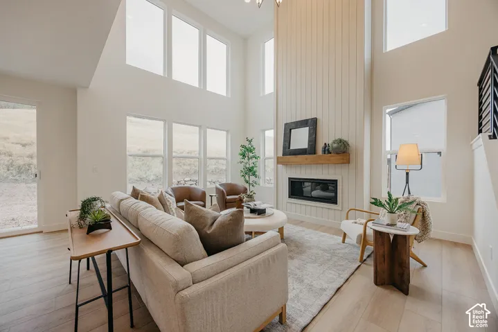Two-story vaulted ceiling with expansive windows, vertical shiplap wall accent, inset gas fireplace, natural wood mantel, and wood-finish flooring