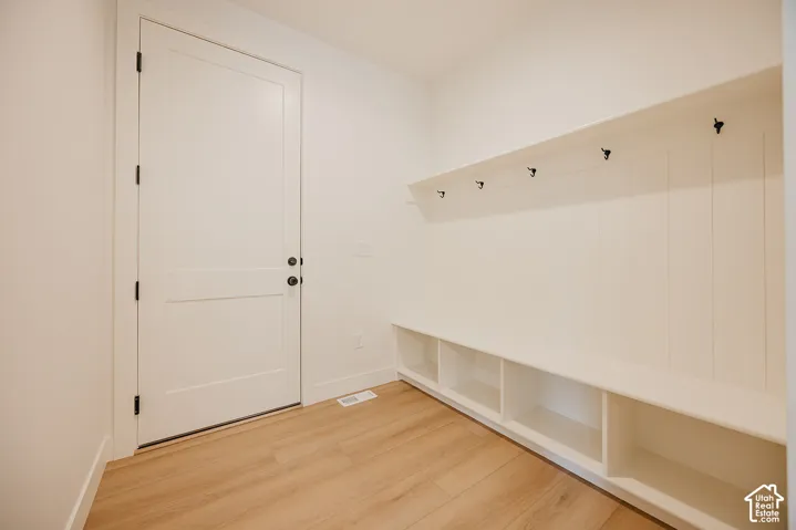 Custom mudroom featuring built-in lower cubbies, a vertical shiplap wall treatment, matte black hardware, integrated shelf, and wood-finish flooring