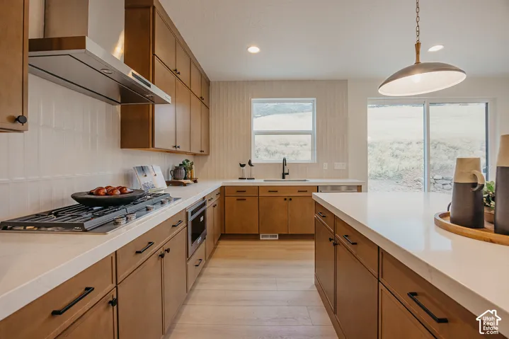 Kitchen featuring stained cabinetry, solid-surface countertops, wood-finish flooring, a stainless steel gas cooktop with matching range hood, and a built-in microwave