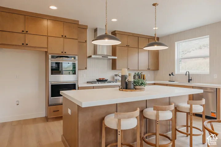 Kitchen featuring wood cabinetry, white stone-surface countertops, stainless steel double wall ovens, a stainless steel range hood, and pendant lighting