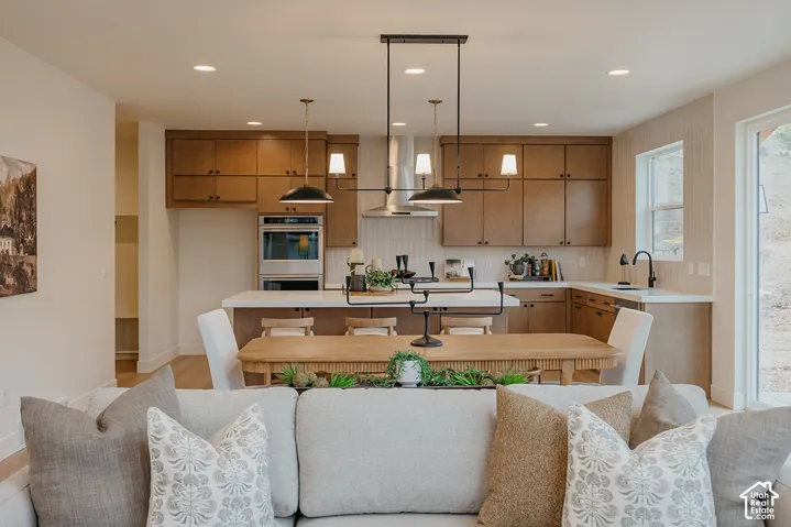 Kitchen featuring custom wood cabinetry, central island with stone countertop, stainless steel double wall oven, sleek range hood, and multi-light pendant fixtures