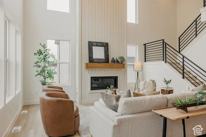 Double-height ceilings, vertical shiplap fireplace surround with a natural wood mantel, wood-finish flooring, and a staircase featuring matte black horizontal railings