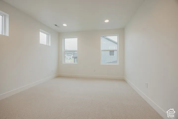 Neutral-toned wall-to-wall carpeting, bright interior paint, recessed lighting, and multiple windows providing natural illumination