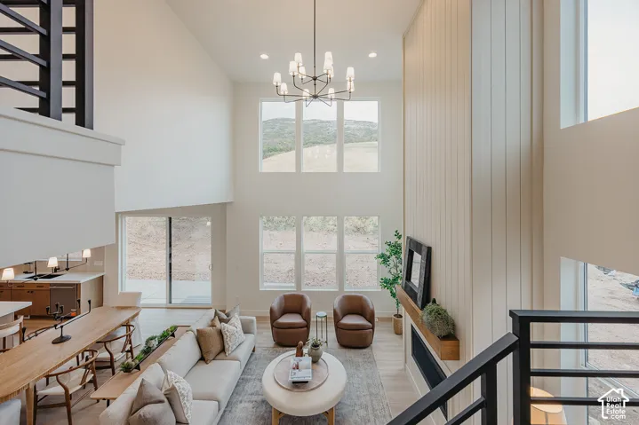 Double-height vaulted ceilings featuring floor-to-ceiling windows, a vertical-plank fireplace surround, a linear mantel, and a multi-arm chandelier