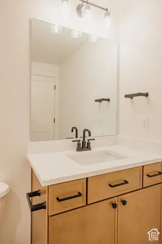 Vanity featuring light wood-finish cabinetry, a stone-composite countertop with an integrated rectangular sink, matte black hardware, a large frameless mirror, and a three-light glass fixture