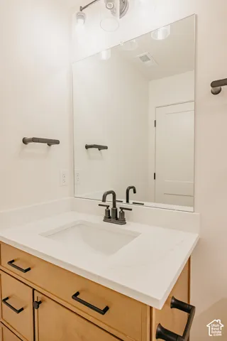 Vanity featuring light wood-finish cabinetry, white countertop, rectangular undermount sink, matte black widespread faucet, and matching hardware