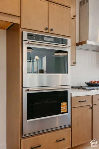 Built-in stainless steel double wall oven, custom wood cabinetry, matte black hardware, white solid-surface countertops, and vertical subway tile backsplash