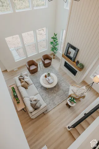 Double-height ceiling, floor-to-ceiling vertical paneled fireplace surround, linear electric fireplace with wood-finish mantel, large multi-pane windows, and light wood-finish flooring