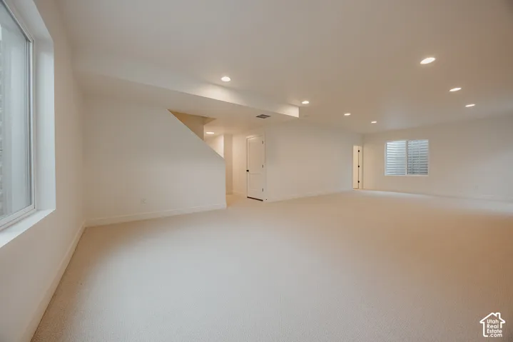 Expansive open-concept room featuring neutral wall-to-wall carpeting, recessed ceiling lighting, and multiple windows
