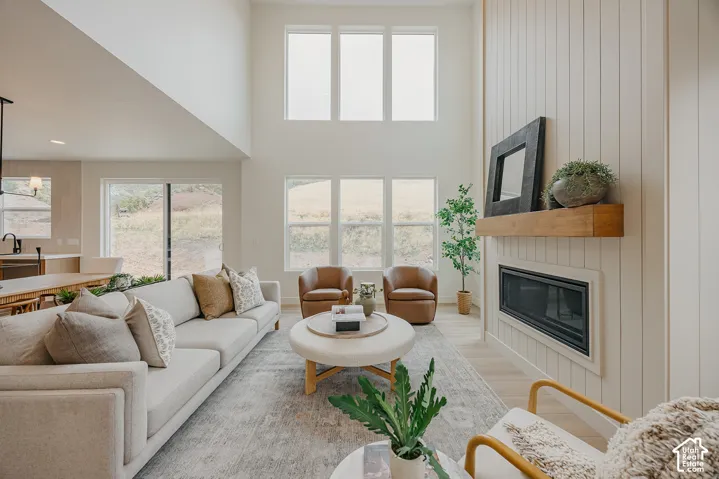 Double-height ceilings featuring large windows, floor-to-ceiling vertical plank wall cladding, and a linear fireplace with a natural wood mantel
