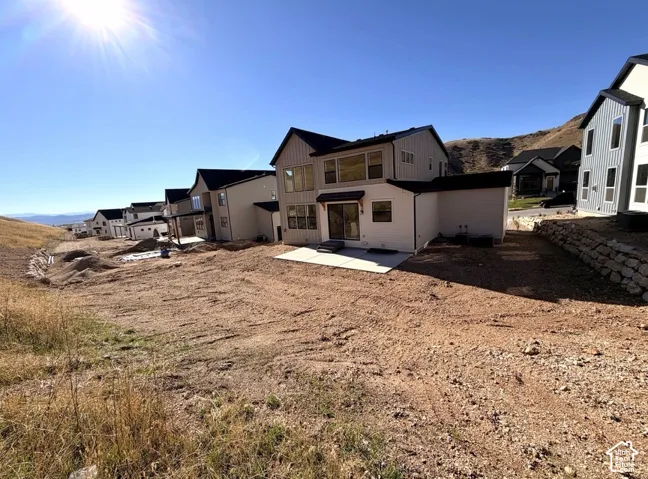 Two-story exterior with vertical and horizontal siding, concrete rear patio, mountain backdrop, and tiered stone retaining wall