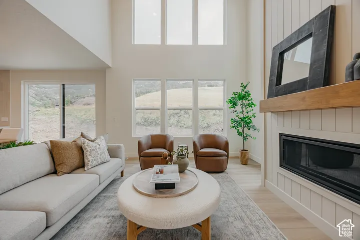 Double-height ceiling featuring oversized windows, floor-to-ceiling board and batten accent wall, recessed fireplace with wood mantel, and wood-finish flooring