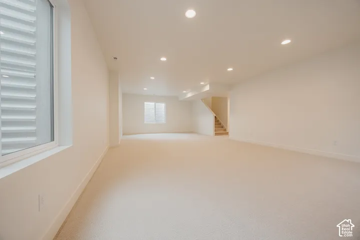 Open-concept interior featuring neutral wall-to-wall carpeting, recessed ceiling lighting, and large windows with horizontal blinds