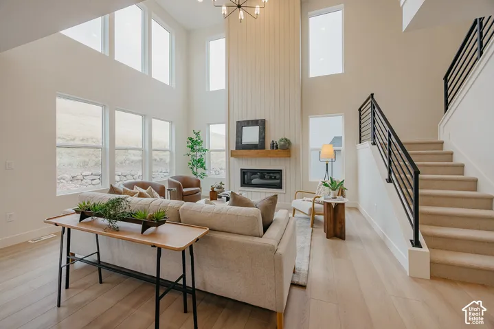 Living area featuring two-story vaulted ceilings, vertical shiplap fireplace surround with a natural wood mantel, abundant oversized windows, wood-finish flooring, and a staircase with a matte black metal railing