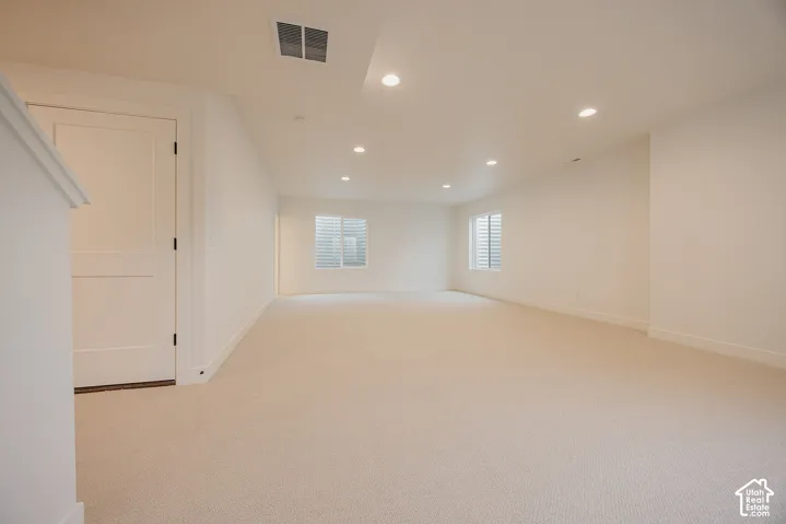 Neutral-toned interior space featuring recessed ceiling lighting, wall-to-wall carpeting, two multi-pane windows, and a solid-core panel door