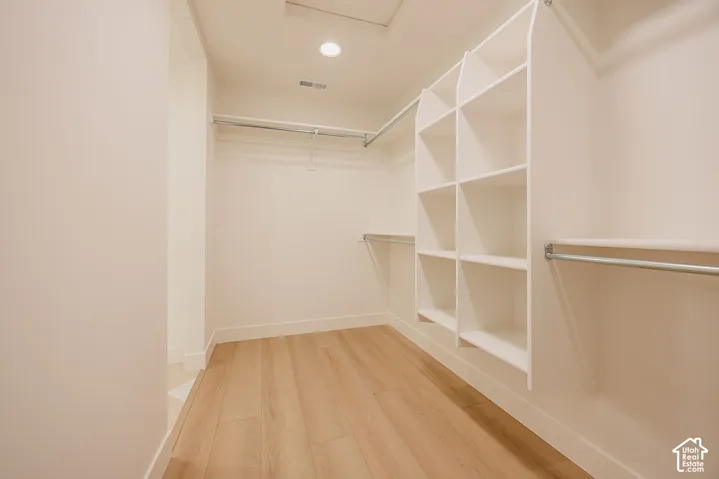 Walk-in closet featuring white built-in shelving, metal garment rods, recessed lighting, and wood-finish flooring