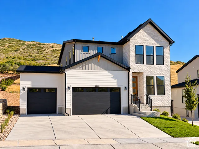 Multi-story exterior featuring white brick and horizontal siding, dark-framed windows, a multi-car garage, and concrete driveway