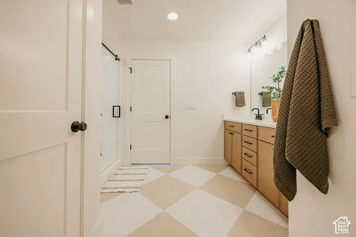 Bathroom featuring a vanity with wood-finish cabinetry, a white countertop, and matte black hardware, paired with a glass-enclosed shower and geometric-patterned flooring