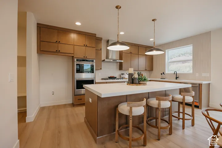 Kitchen featuring flat-panel wood cabinetry, a central island with white stone countertop, built-in stainless steel double wall ovens, wood-finish flooring, and dual industrial-style pendant light fixtures