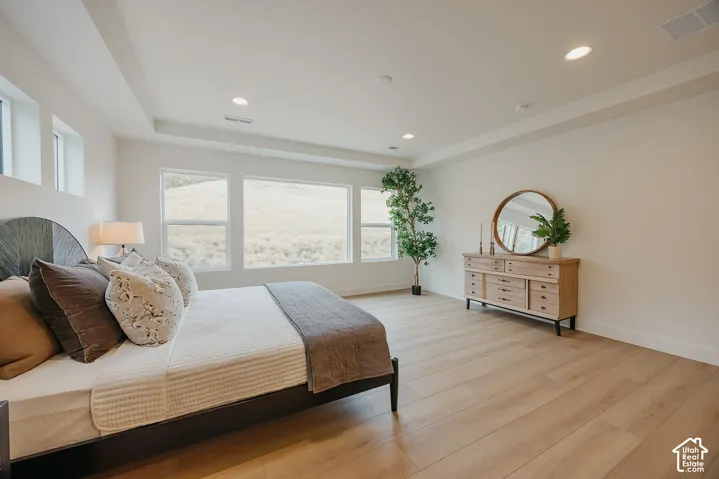 Spacious room featuring wood-finish flooring, recessed lighting, a stepped ceiling, and large windows with landscape scenery