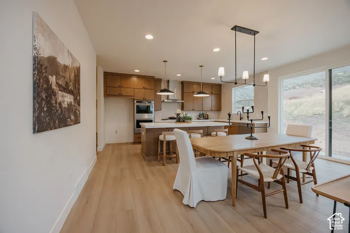 Kitchen featuring wood-finish cabinetry, built-in double wall ovens, a large island with quartz countertops, wood-finish flooring, and a linear multi-light pendant fixture