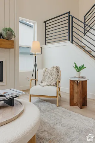 Staircase featuring matte black horizontal metal railings, light wood-finish flooring, vertical wall paneling, and a natural wood mantelpiece