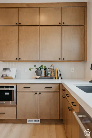 Custom wood-finish flat-panel cabinetry with matte black hardware, white solid-surface countertops, vertical-tile backsplash, and integrated stainless steel microwave