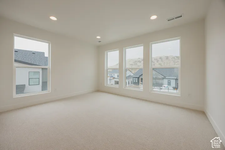 Neutral-toned interior space featuring light-colored wall-to-wall carpeting, high-reaching windows, and recessed lighting
