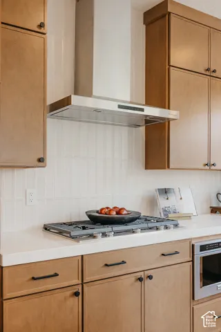 Kitchen featuring flat-panel wood cabinetry with matte black hardware, white solid-surface countertops, vertical tile backsplash, stainless steel gas cooktop, and a matching stainless steel range hood
