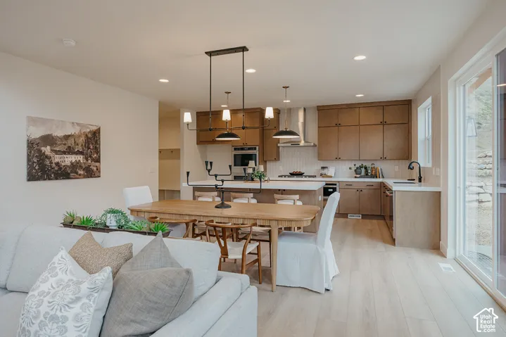 Kitchen featuring wood-finish cabinetry, quartz countertops, a stainless steel wall oven, an integrated range hood, and wood-finish flooring