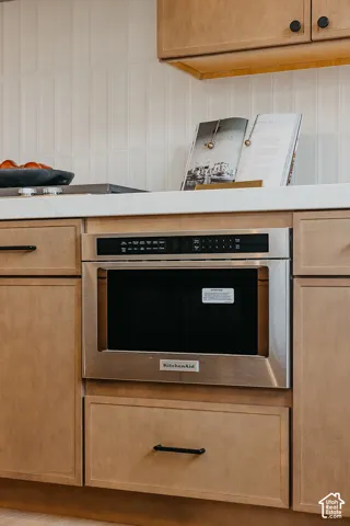 Custom flat-panel wood cabinetry featuring matte black hardware, built-in stainless steel microwave drawer, white stone countertop, and vertical tile backsplash