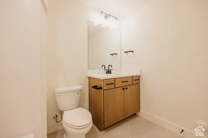 Bathroom featuring wood-finish vanity cabinetry with matte black hardware, white countertop with integrated sink, rectangular wall-mounted mirror, and tile flooring