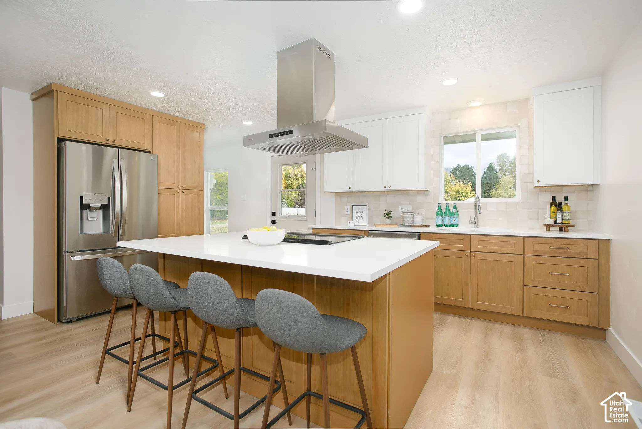 Kitchen featuring two-tone cabinetry, a central island with a quartz countertop, stainless steel appliances, a ceiling-mounted range hood, and light-toned wood-finish flooring