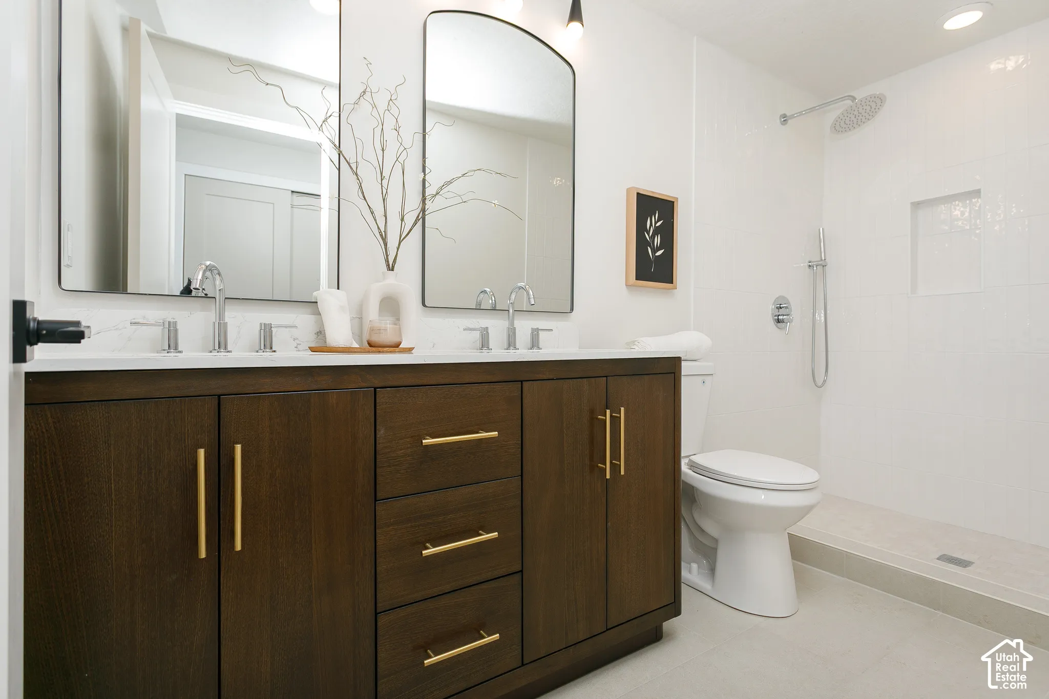 Dark wood-finish vanity with gold-tone hardware, white countertop, dual arched mirrors, and a walk-in shower with white tile surround and recessed niche
