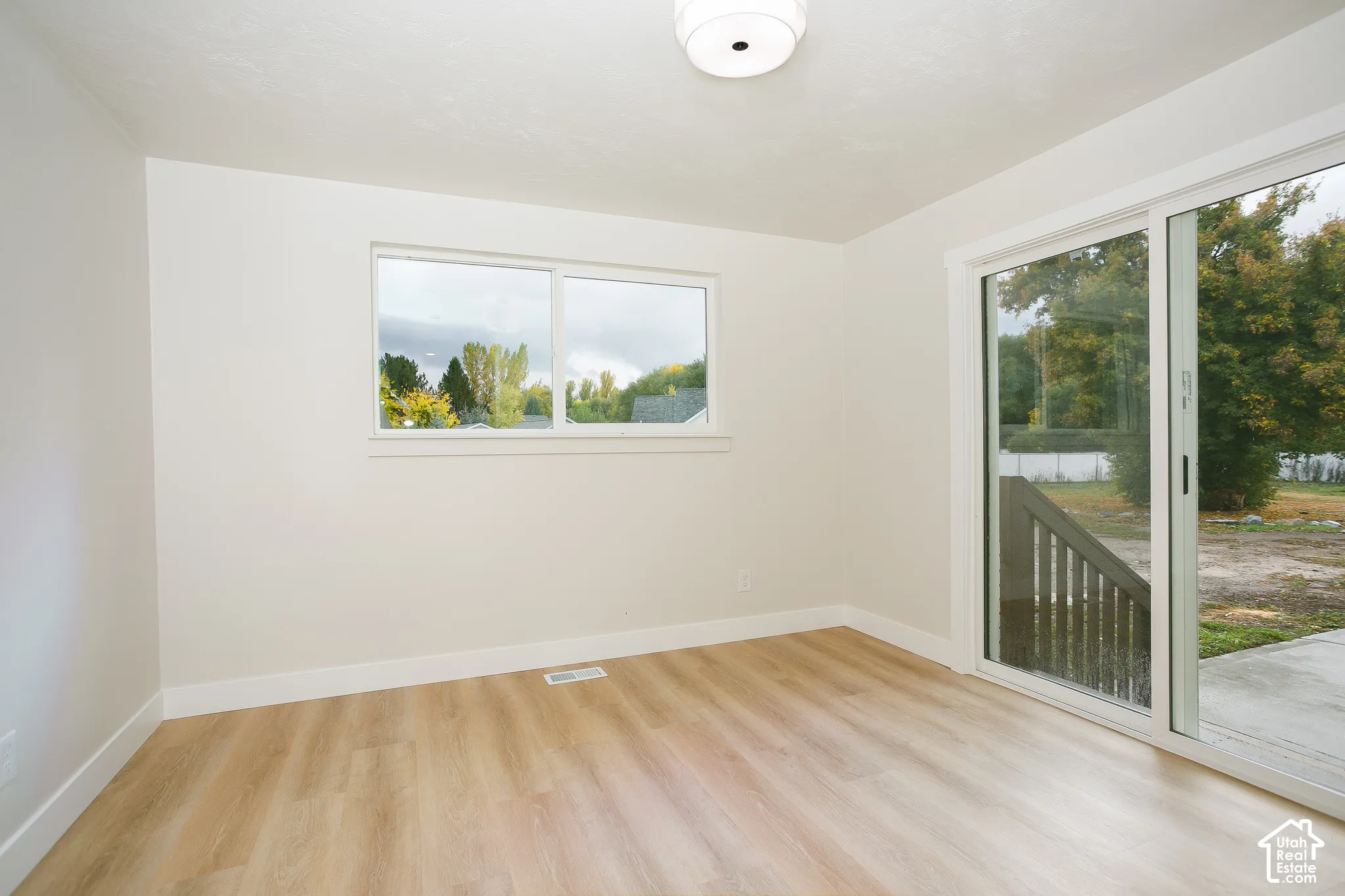 Room featuring wood-finish flooring, neutral wall paint, a double-pane horizontal window, a flush-mount light fixture, and sliding glass doors opening to an exterior concrete patio
