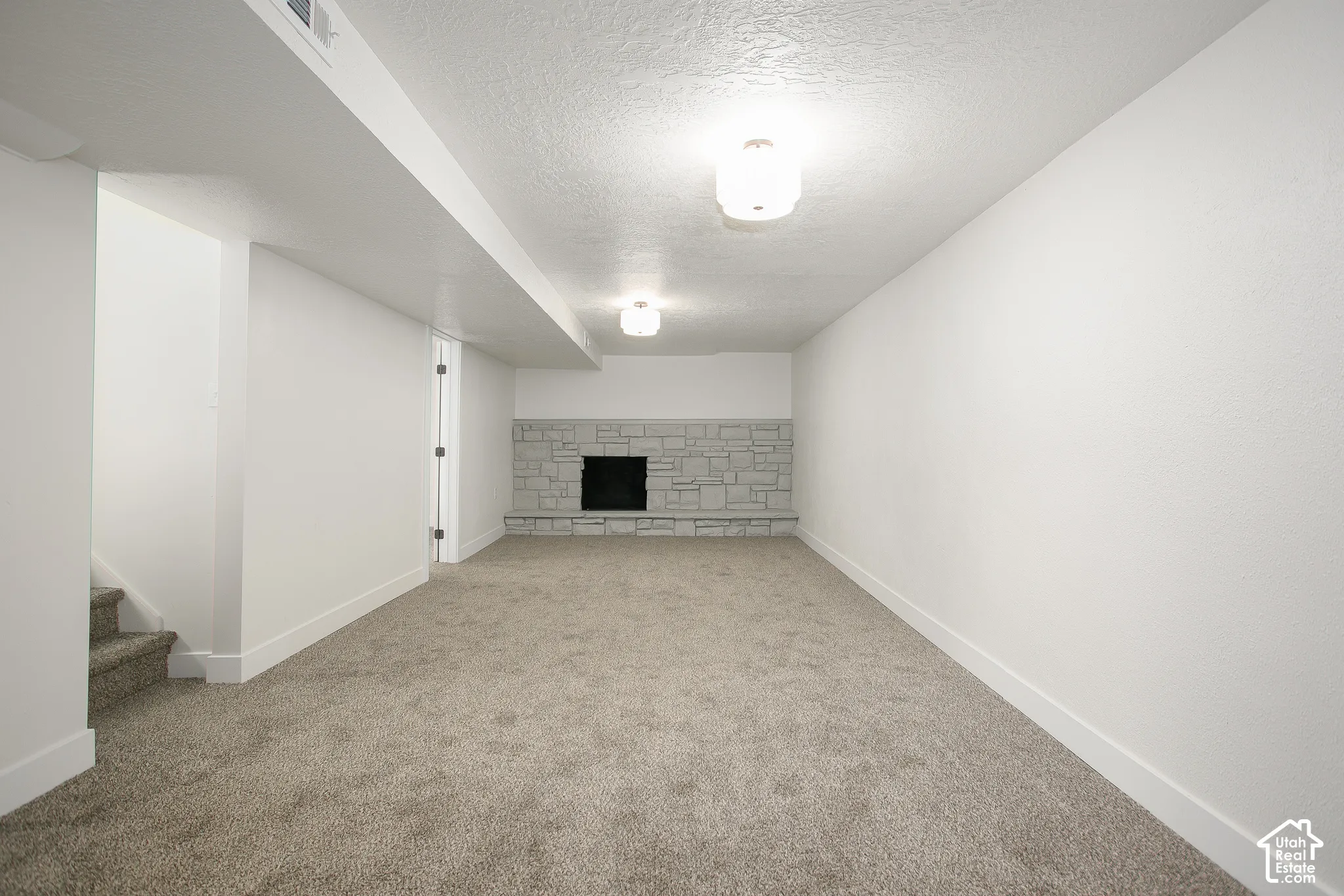 Neutral-toned interior space featuring stone-surround fireplace, textured carpet flooring, and dual flush-mount ceiling fixtures