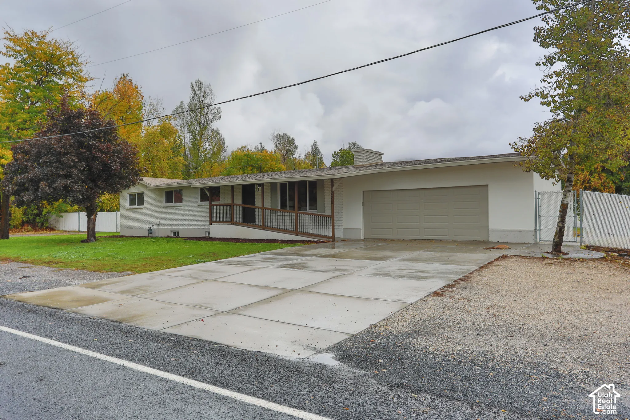 Single-story exterior featuring a light-colored masonry finish, attached multi-car garage, concrete driveway, and a covered porch with wooden railings